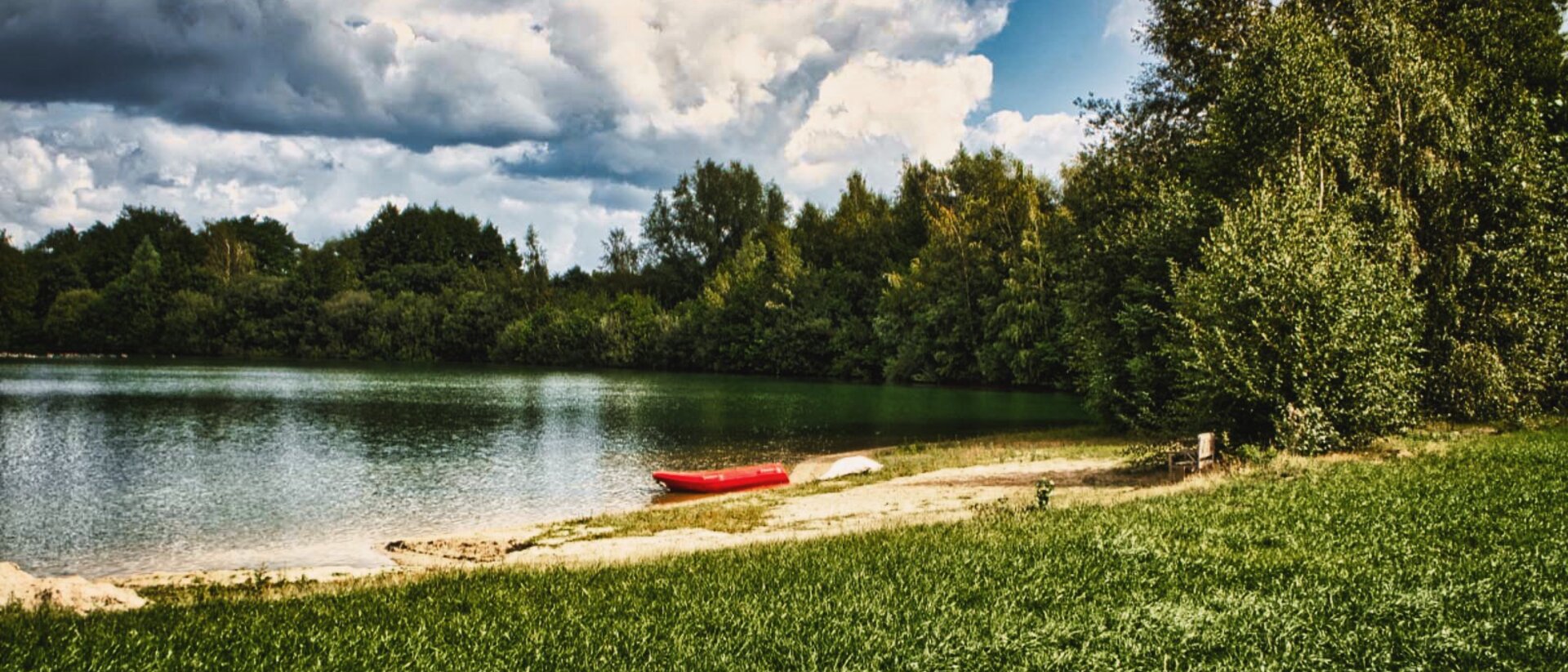 Kleiner See mit Boot am Ufer und Bäumen im Hintergrund