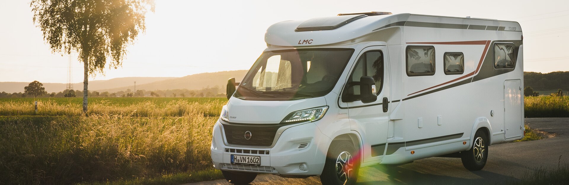 LMC Wohnmobil auf Landstraße mit tief stehender Sonne im Hintergrund