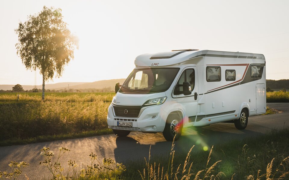 LMC Wohnmobil auf Landstraße mit tief stehender Sonne im Hintergrund