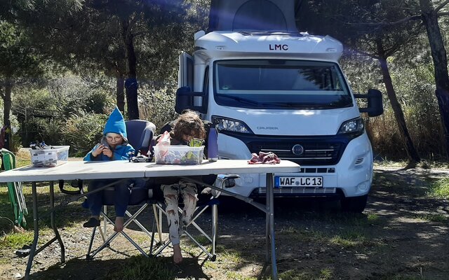 Zwei Kinder basteln am Tisch, im Hintergrund steht der LMC Camper