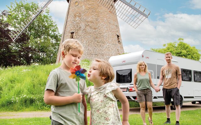 Familie mit zwei Kindern vor LMC-Wohnwagen, Windmühle im Hintergrund