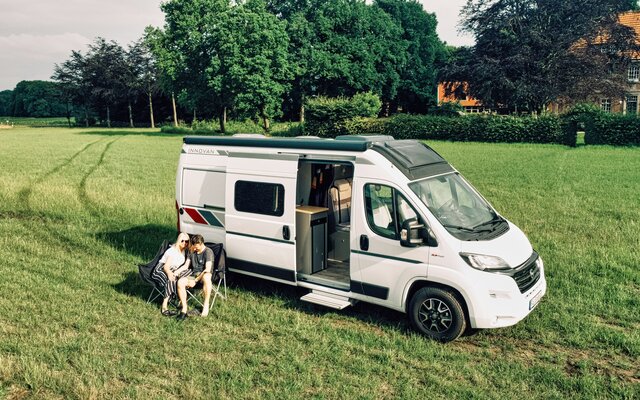 LMC Wohnmobil auf einer Wiese, davor sitzt ein Pärchen