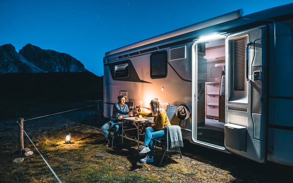 Paar vor Wohnmobil im Kerzenschein mit Wein