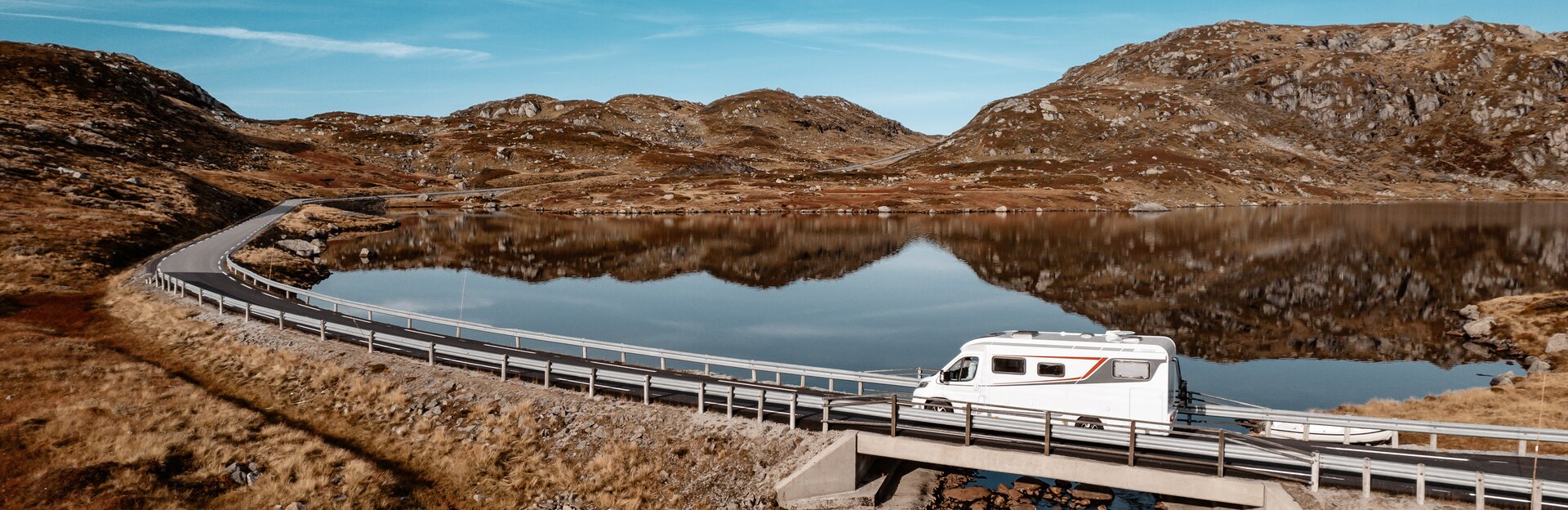 Wohnmobil auf Brücke im Hintergrund Berge und Wasser