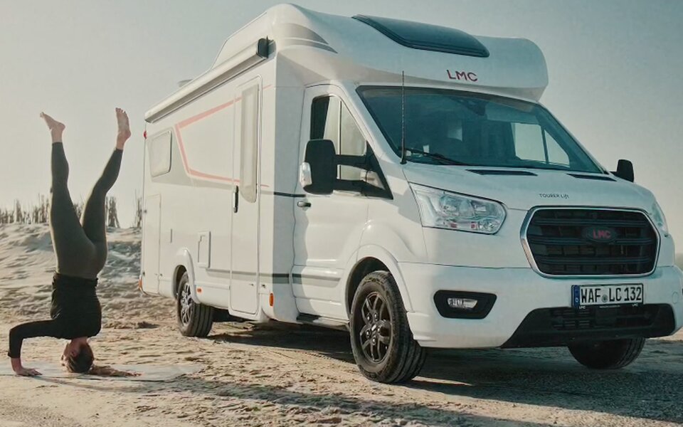 Frau am Strand im Kopfstand mit LMC Wohnmobil