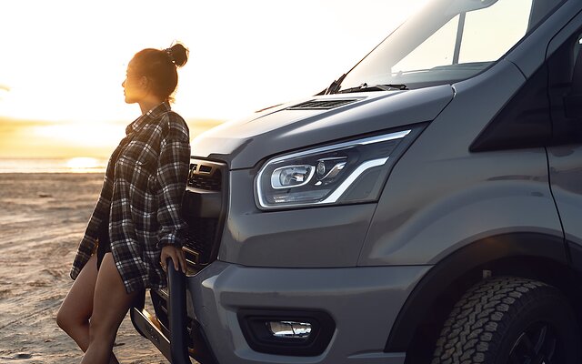 Frau vor LMC Wohnmobil am Strand mit Sonnenuntergang