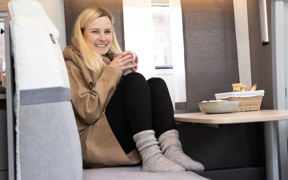 Frau mit Tasse und Kuschelsocken auf LMC Sitzgarnitur im Wohnmobil