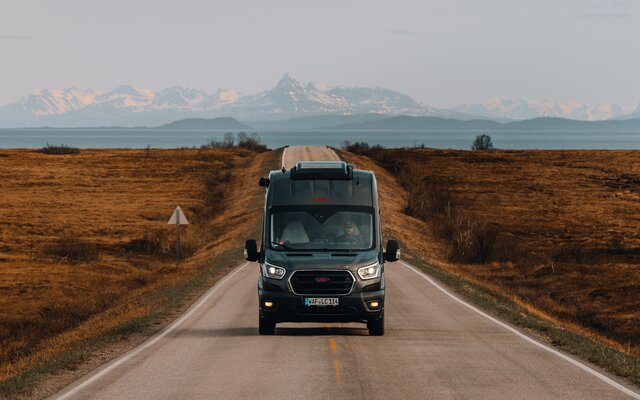 LMC Innovan Camper Van fährt in Norwegen auf langer, gerader Straße mit imposanten Bergen im Hintergrund.
