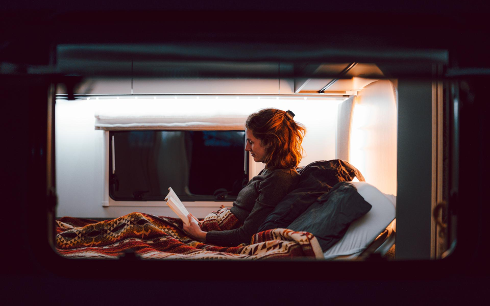 Eine Frau liegt im Bett und ließt ein Buch im LMC Wohnwagen Videro.